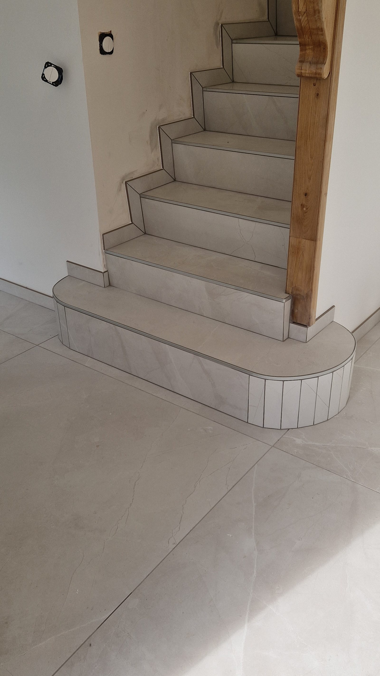 Escalier carrelé effet marbre avec baguettes de finition métalliques et marche arrondie en pied