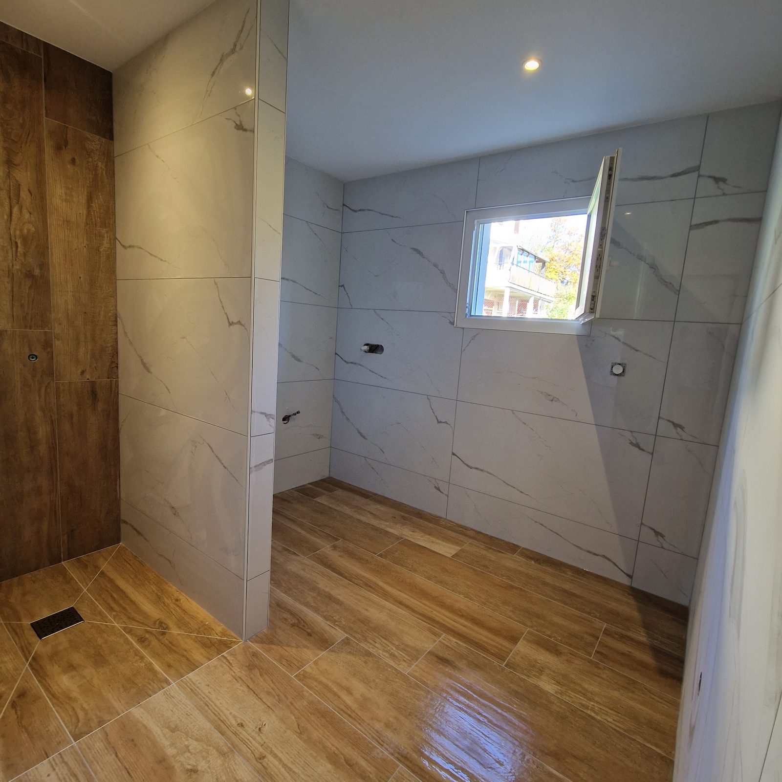 Vue d'ensemble d'une salle de bain rénovée mariant effet marbre et carrelage imitation bois