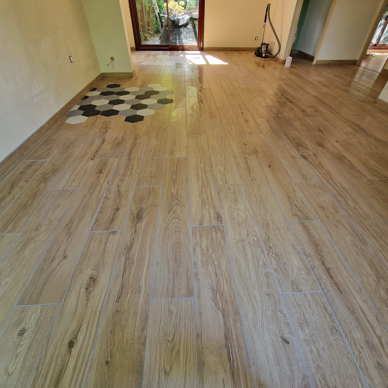 Pose de carrelage effet bois dans une pièce de vie avec médaillon hexagonal noir, blanc et gris au centre