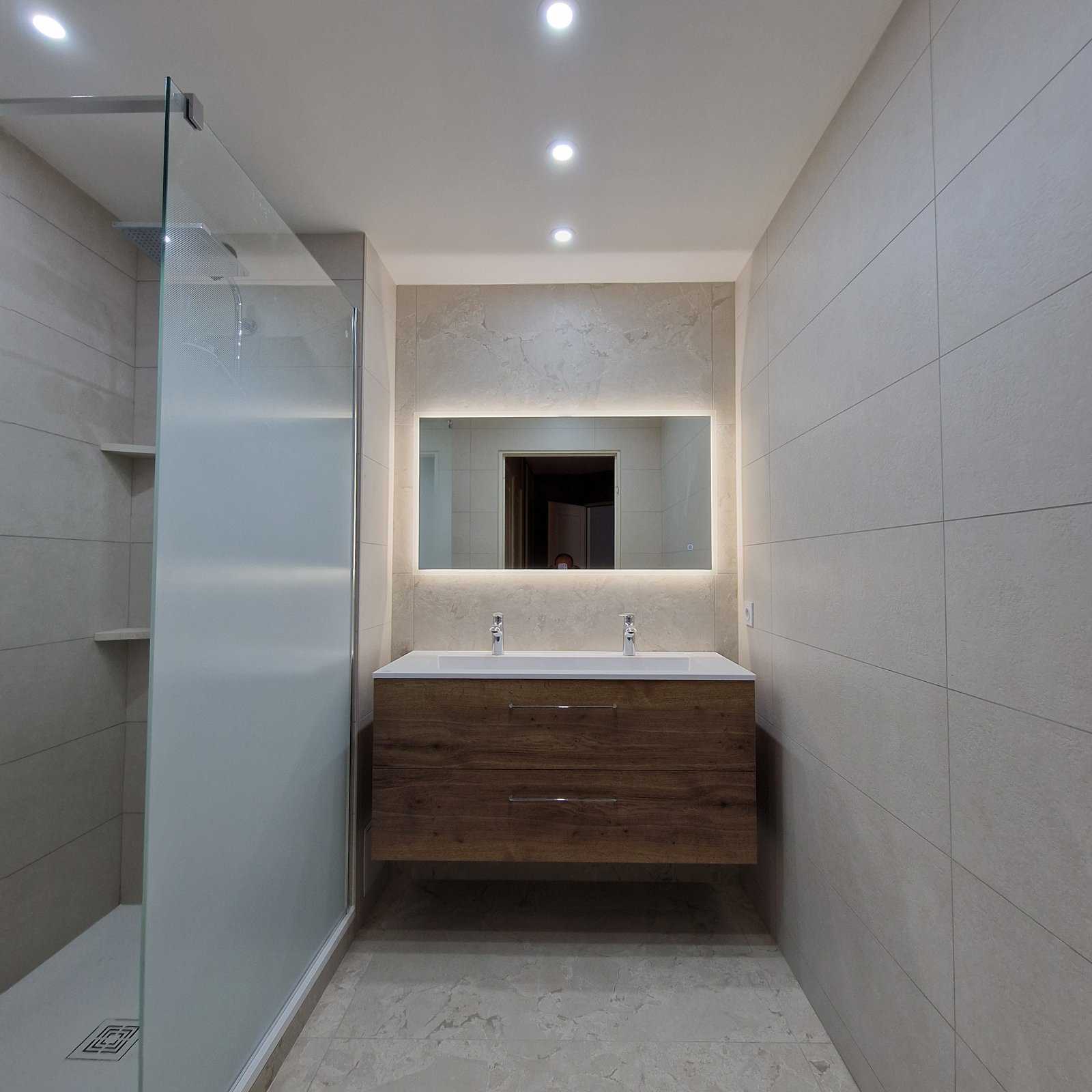 Salle de bain moderne avec double vasque, miroir LED rétroéclairé et meuble bois, réalisée par SR Carrelage à Meylan