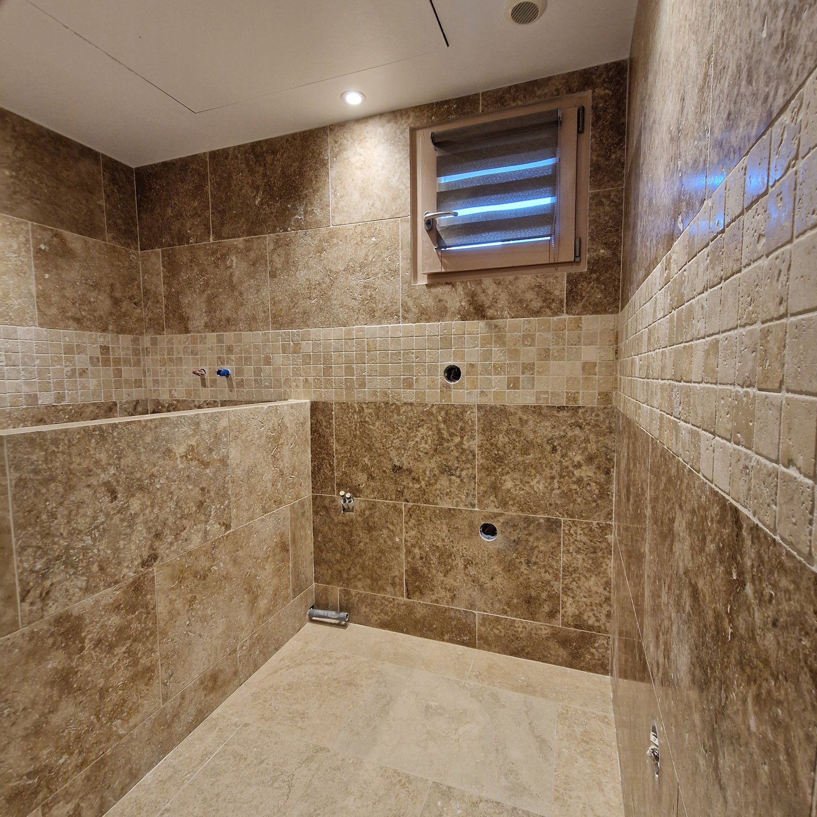 Salle de bain en travertin avec frise mosaïque et grand format, pose en pierre naturelle réalisée en Isère