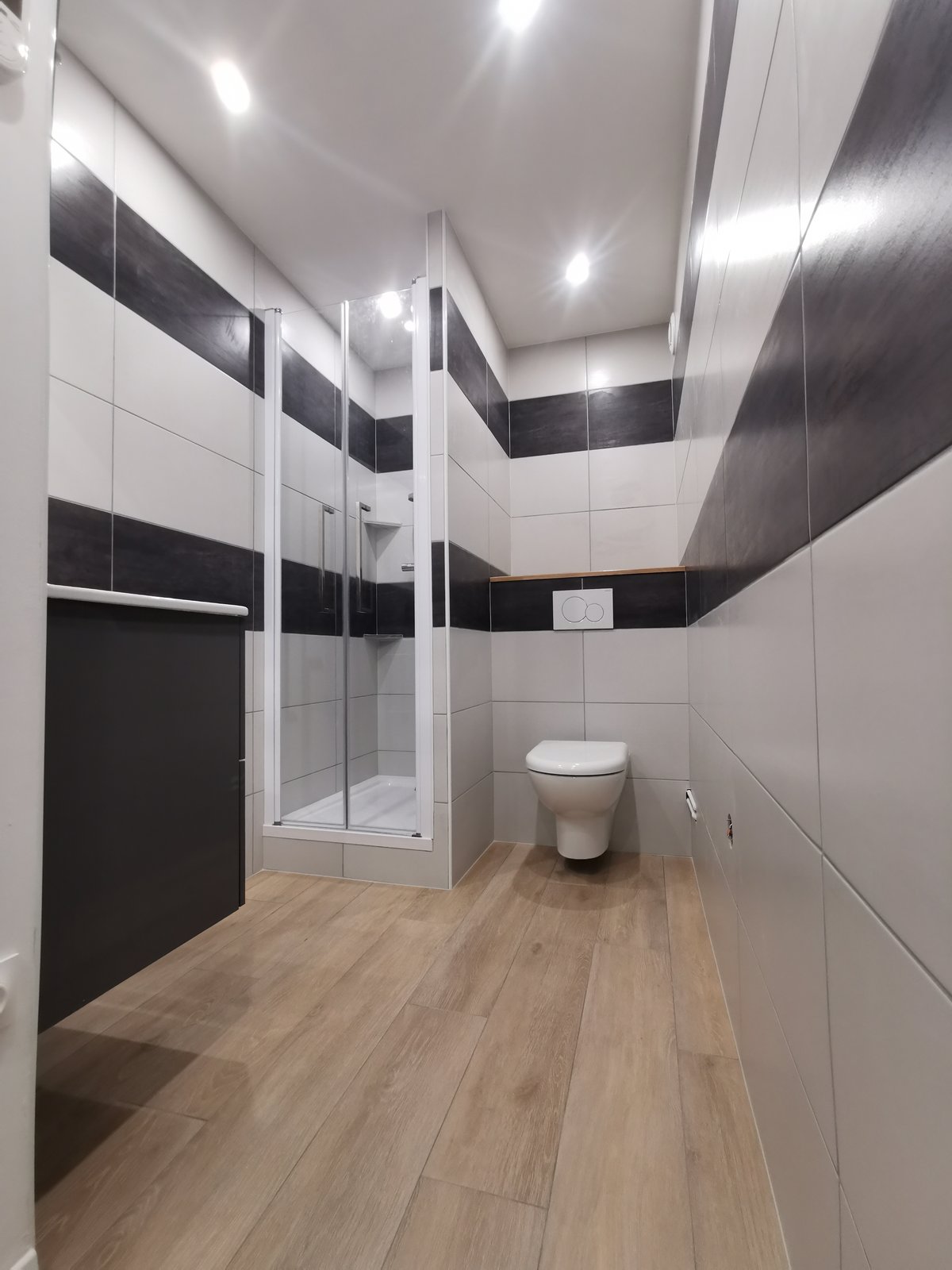 Après : salle de bain épurée avec mosaïque murale décorative noire, WC suspendu, sol bois et carrelage blanc