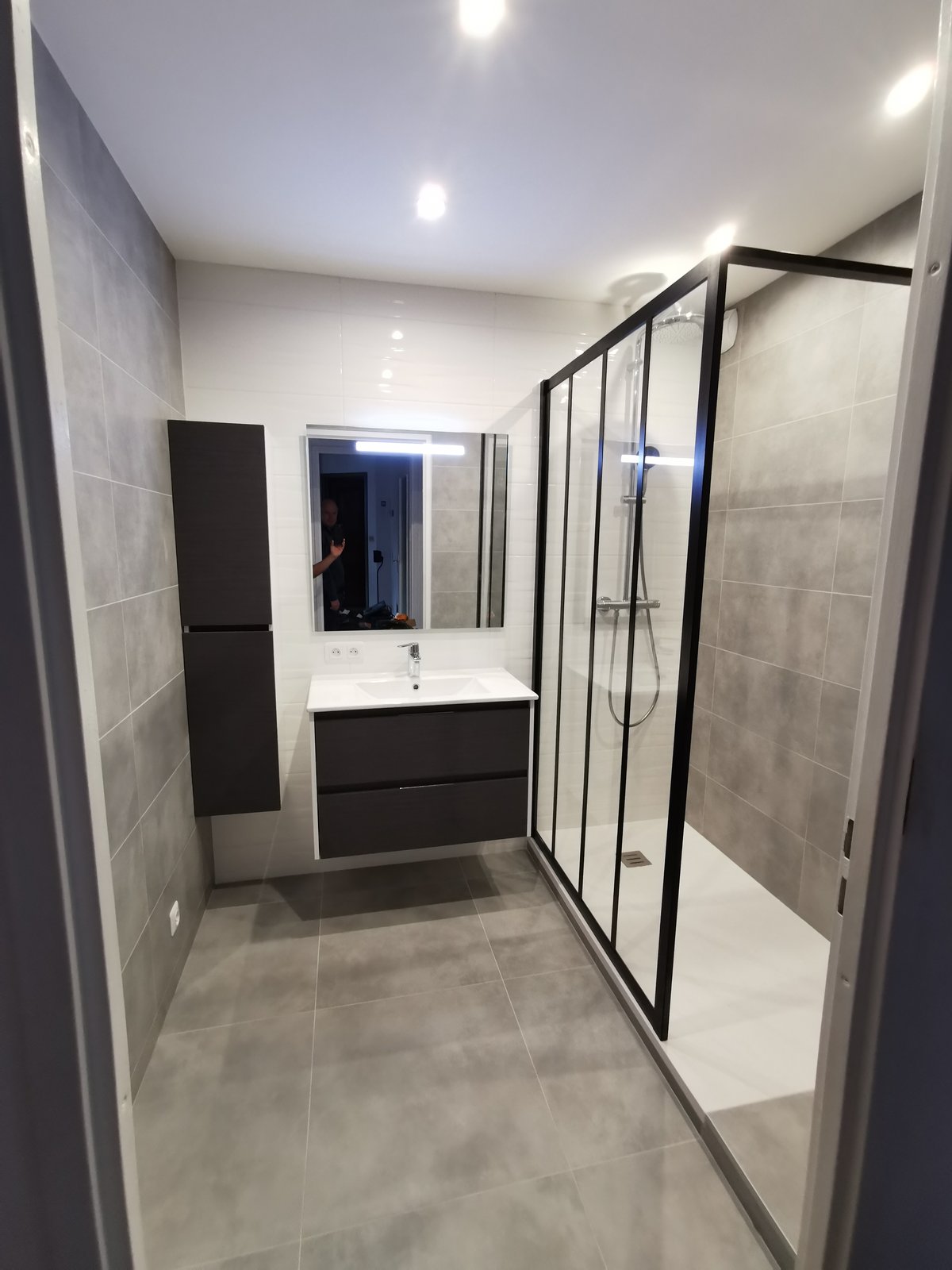 Après : couloir d'eau moderne avec plan vasque, miroir noir, douche, sol effet pierre clair