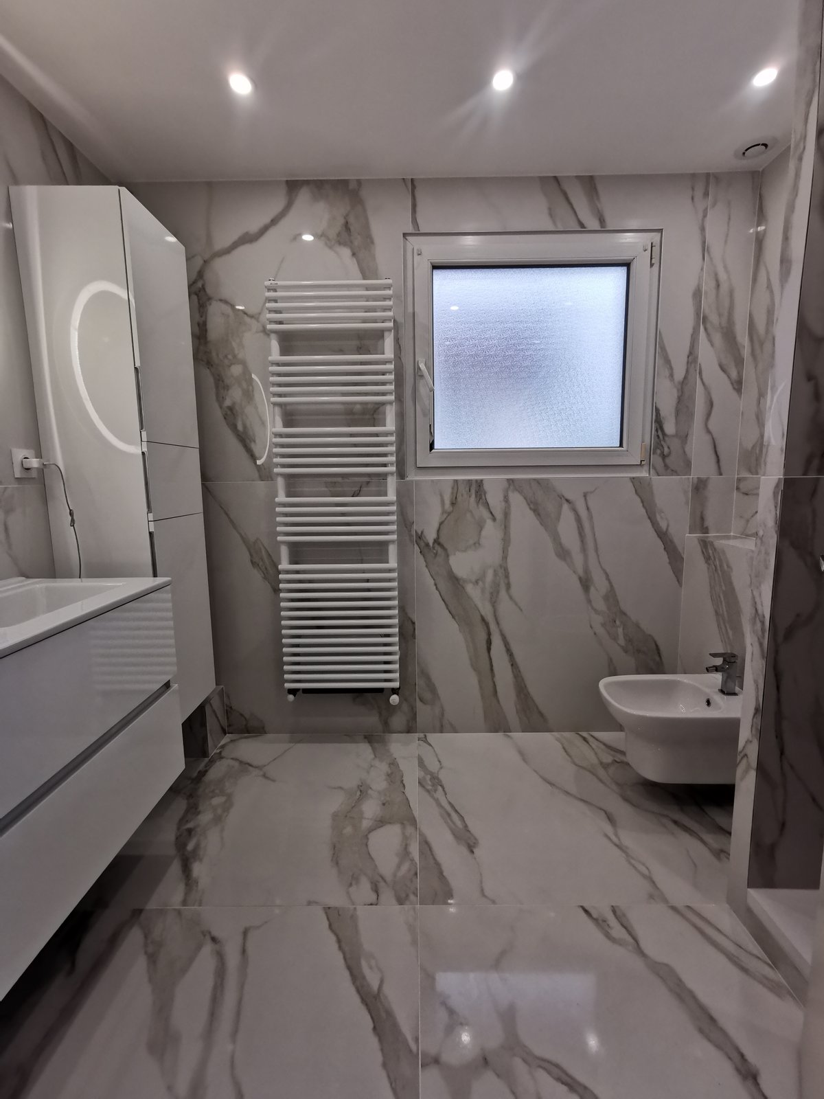 Après : salle de bain entièrement refaite en grand format effet marbre blanc veiné, WC suspendu, radiateur sèche-serviettes design