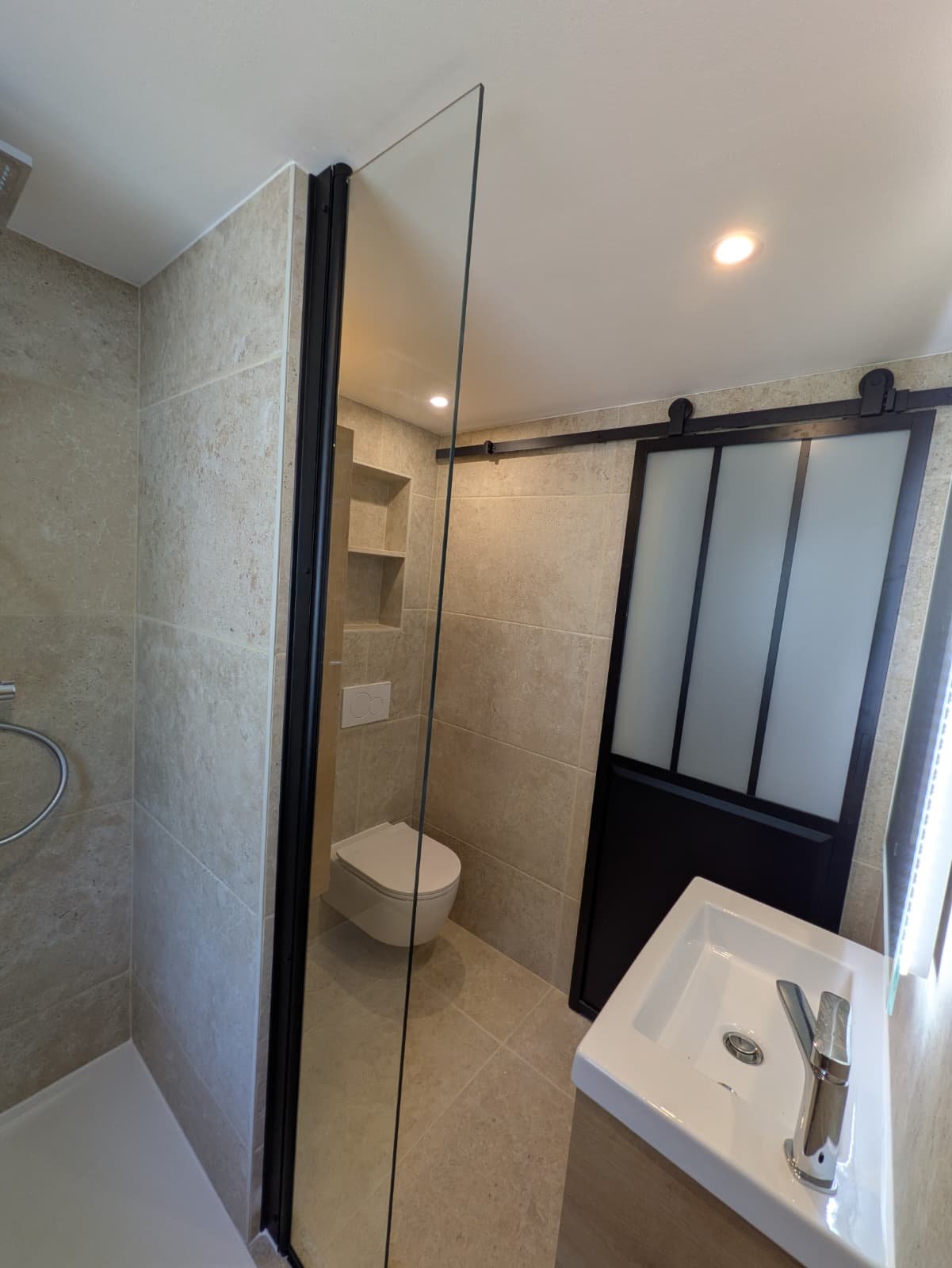 Après : salle de bain rénovée en grand format effet pierre, douche italienne, WC suspendu, porte coulissante style atelier