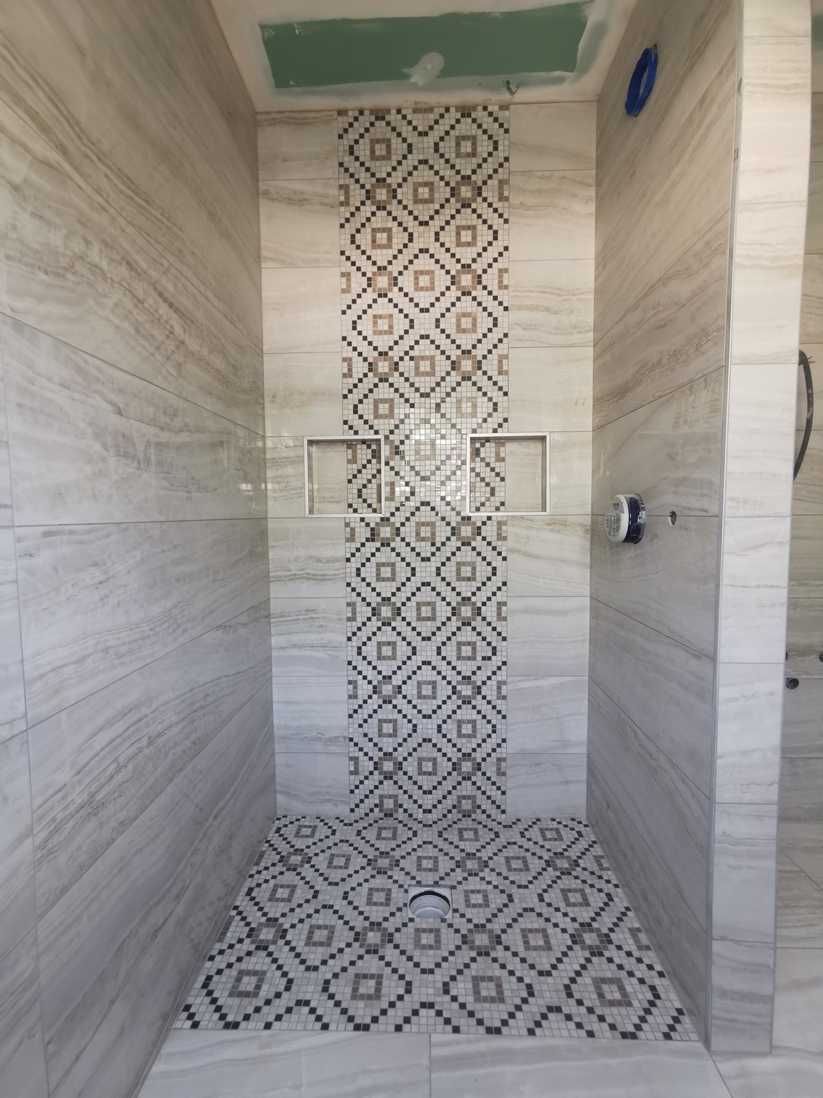 Salle de bain grise avec mosaïque centrale décorative au sol et baignoire