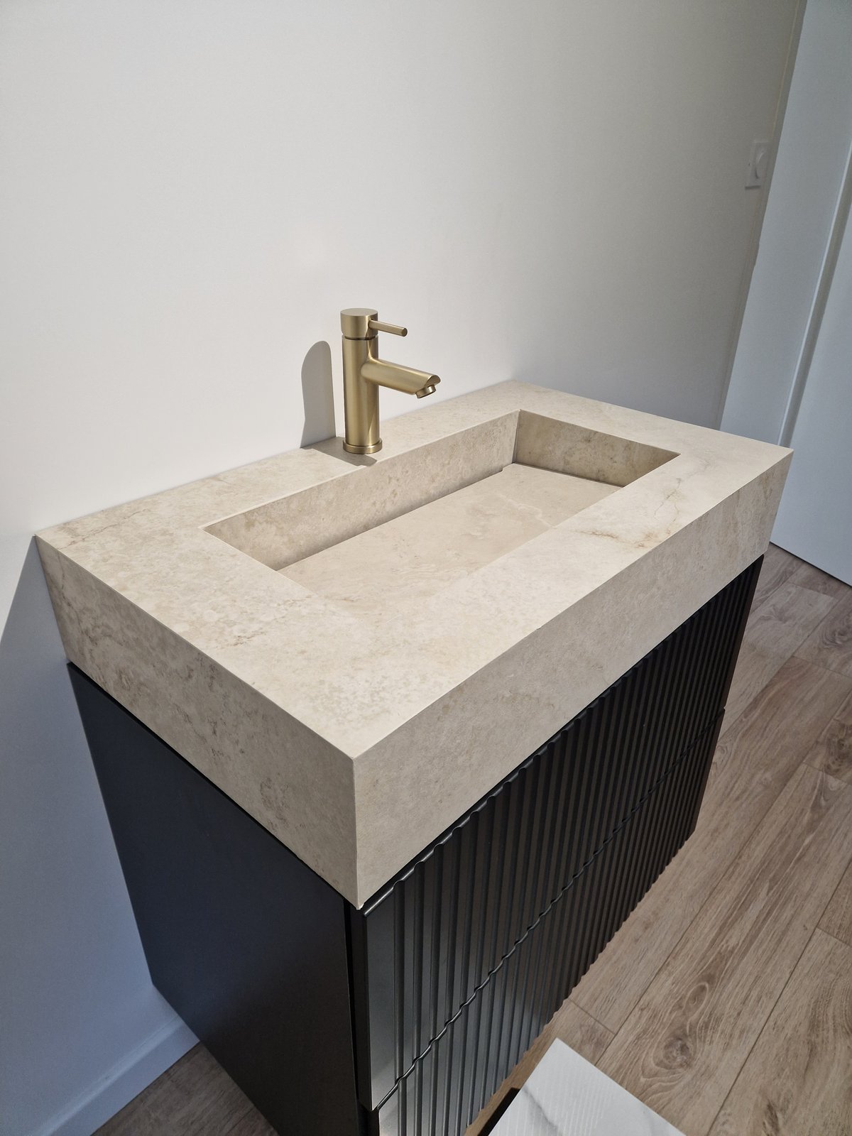 Vasque en carrelage effet travertin clair avec meuble noir cannelé et robinetterie dorée
